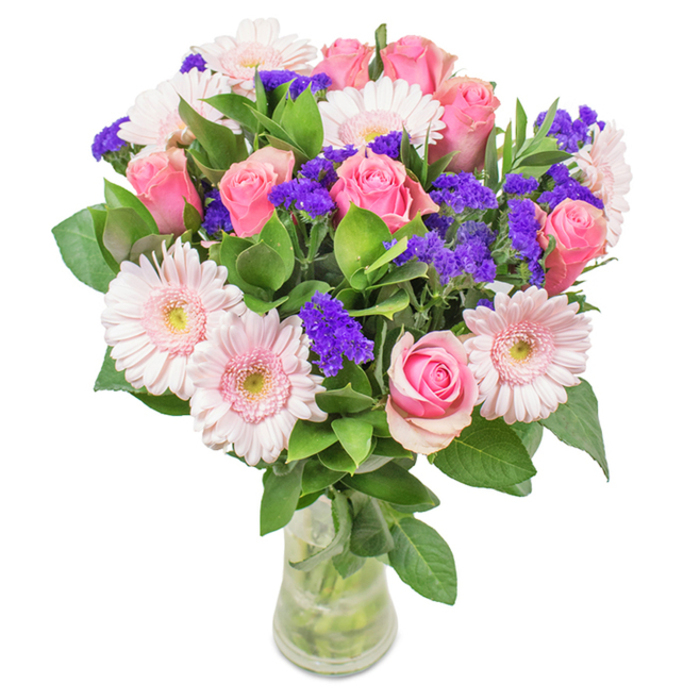 A vibrant, elegantly realized bouquet sits in a crystal-clear glass vase, staged thoughtfully against a clean, white backdrop reminiscent of the airy interiors along Millwall's riverside. The centrepiece features approximately seven to nine exquisite pink roses-some buds tightly closed, others just opening to reveal intricate, spiral petals in hues from soft blush to medium rose. Around them are five to seven pale pink gerbera daisies, easily distinguished by their broad, cheerful faces and lighter, near-white centers, a nod to the delicate pastels of spring in Island Gardens. Throughout the arrangement, clusters of vivid purple statice introduce a lively contrast and intriguing texture, deepening the palette. Lush, deep green foliage provides a verdant foundation, enhancing both the vibrancy and the sense of bouquet abundance. Stems are gracefully visible through the vase and caught in clear, fresh water, evoking thoughts of same-day delivery from Millwall's trusted local florists. Designed to suit birthdays, Mother's Day, or special moments celebrated in Docklands apartments and family homes alike, this bouquet blends classic elegance with a contemporary Millwall touch-conveying joy, celebration, and genuine affection.